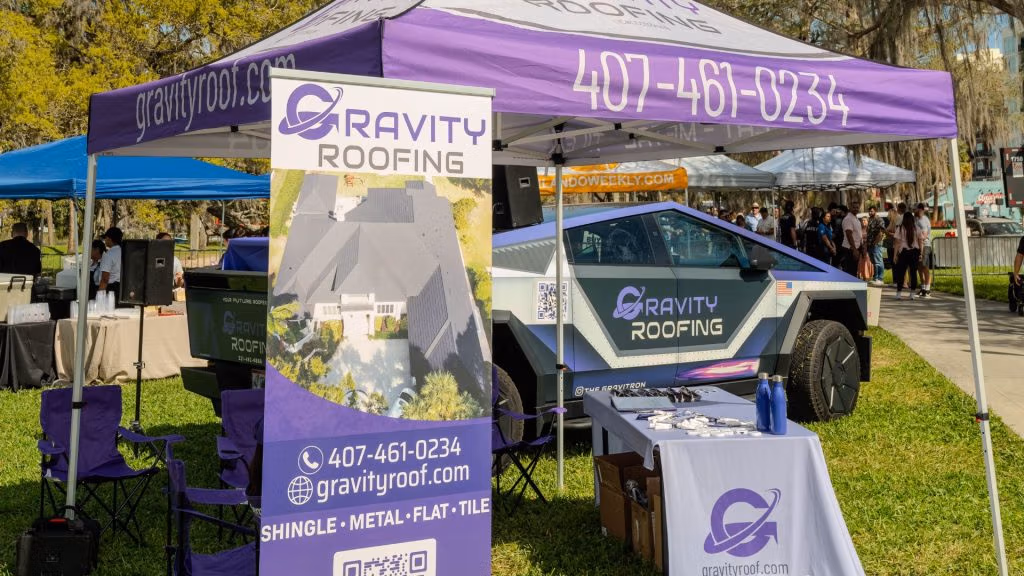 Gravity Roofing booth at Brunch in the Park 2025 in Orlando, FL, featuring The Gravitron vehicle, branded canopy, and community outreach setup