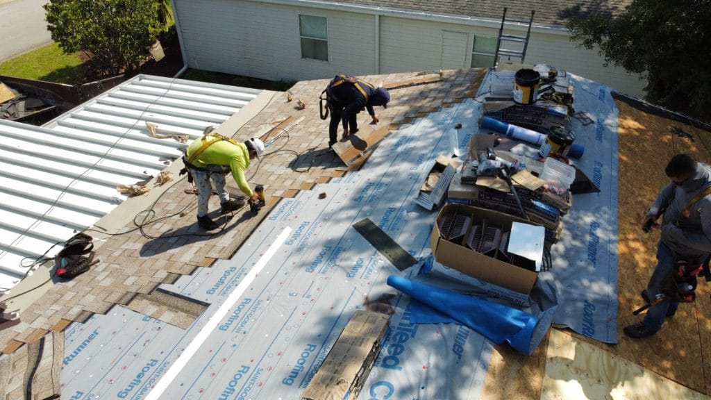 Roofers repairing shingles and underlayment on a house roof after storm damage