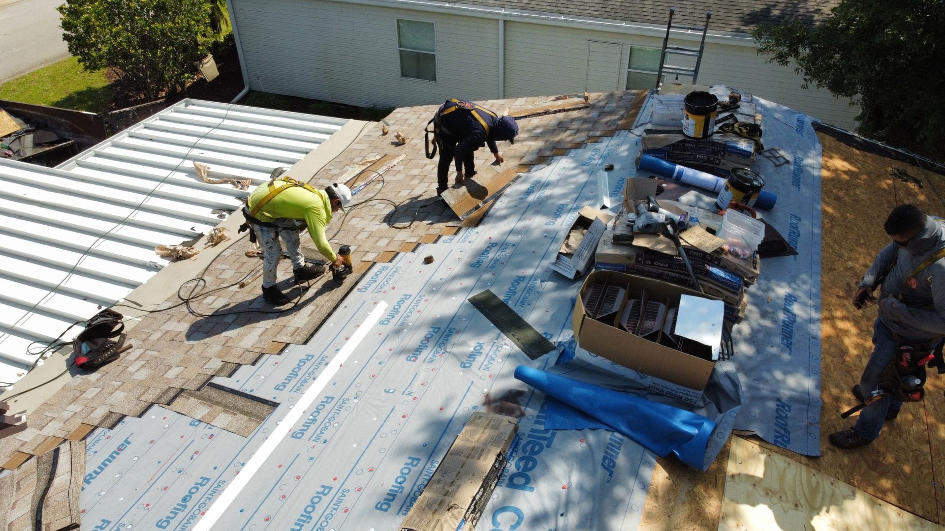 Roofers repairing shingles and underlayment on a house roof after storm damage