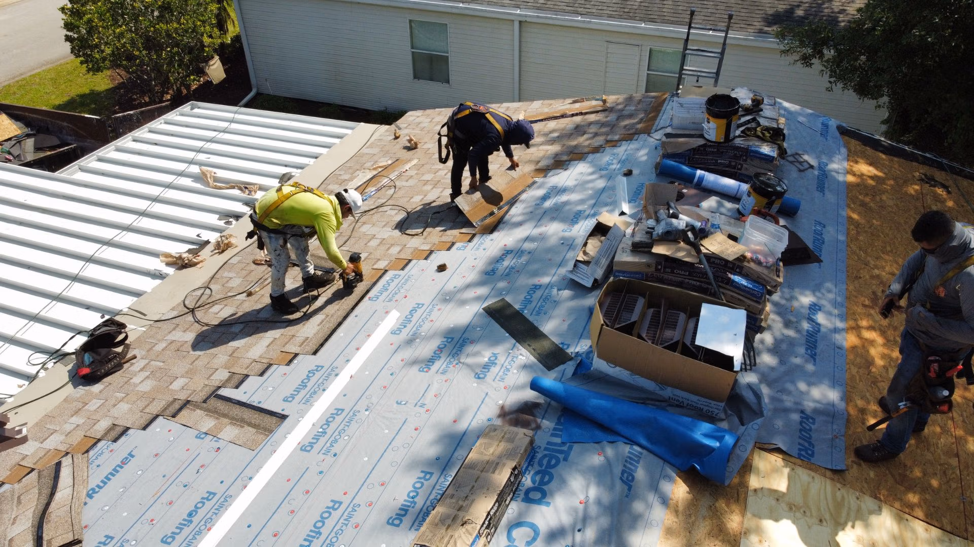 Roofers repairing shingles and underlayment on a house roof after storm damage
